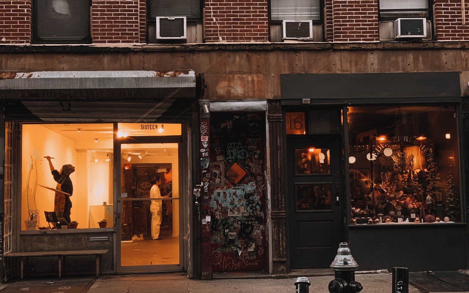 Opening-night crowd on a Chelsea sidewalk — adults spilling out of a gallery doorway in the evening, roll-down shutters visible either side