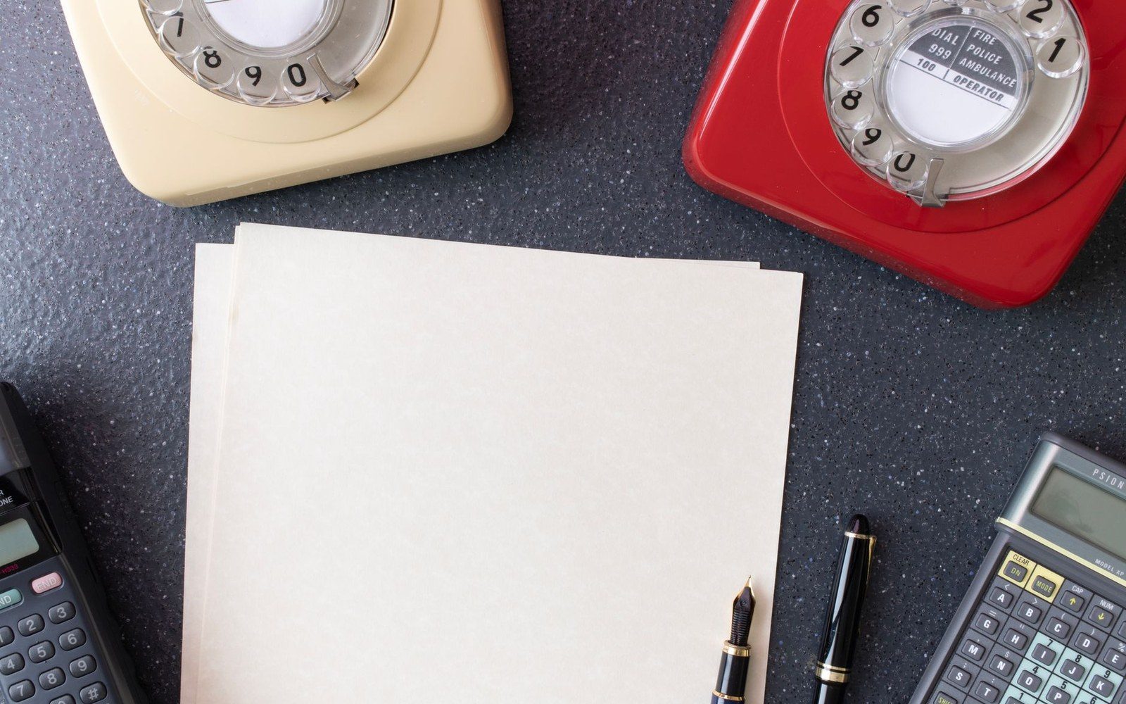 Dealer at a desk in a gallery office — adult figure, slide sheets and a ledger open, telephone, framed work leaning against the wall behind