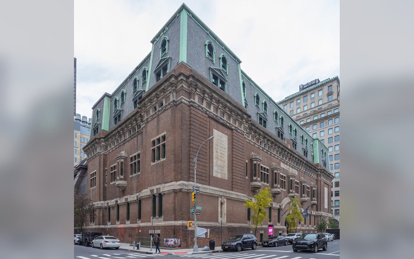 Brick armory building with a green mansard roof and dormer windows on a city corner