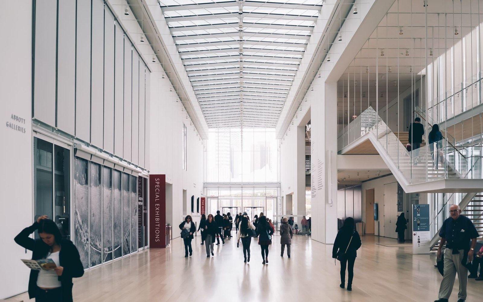 Visitors walk through a bright museum atrium with a glass ceiling and staircase