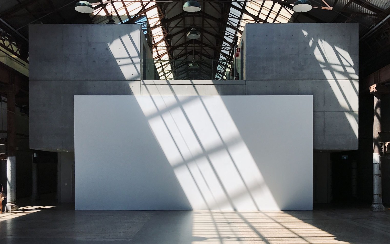 Sunlight streams through a glass roof, casting window shadows on a white gallery wall