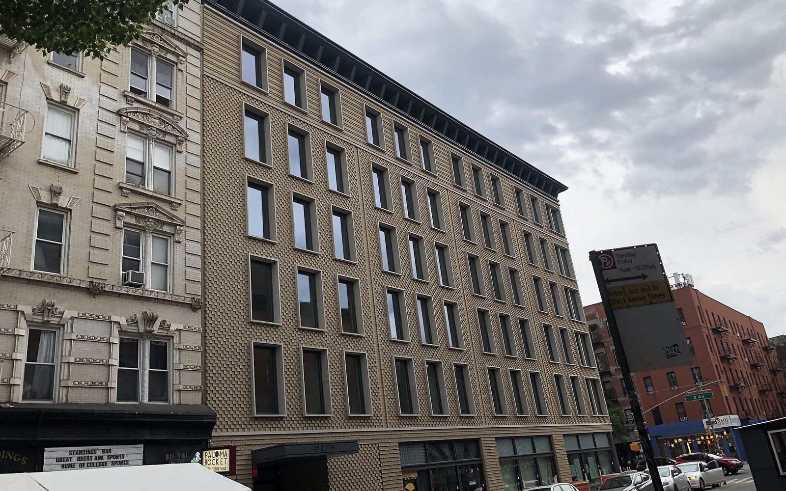 A tan brick apartment building stands beside an older ornate facade on a city street