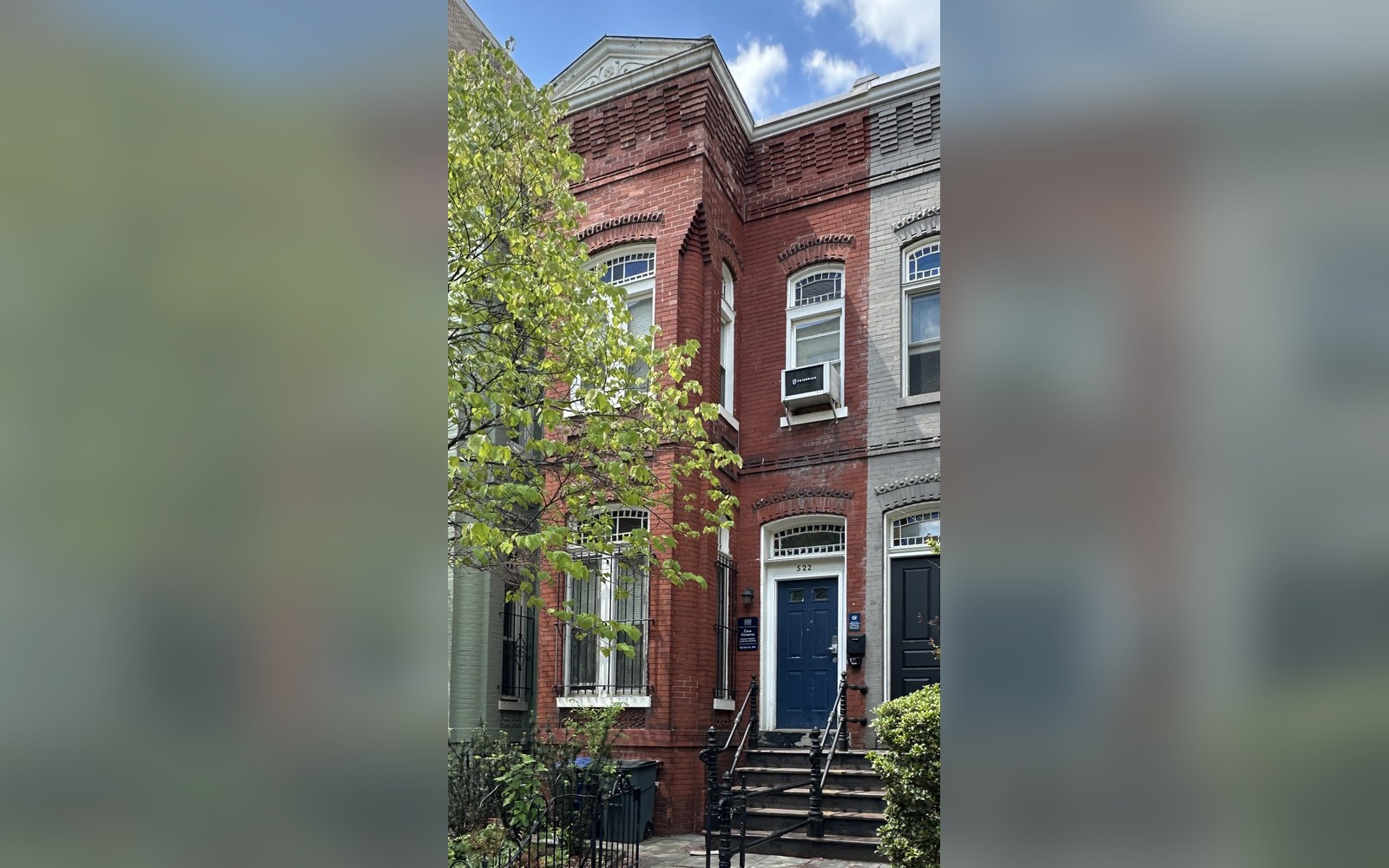 Brick row house with a blue front door, stone steps and a leafy tree out front