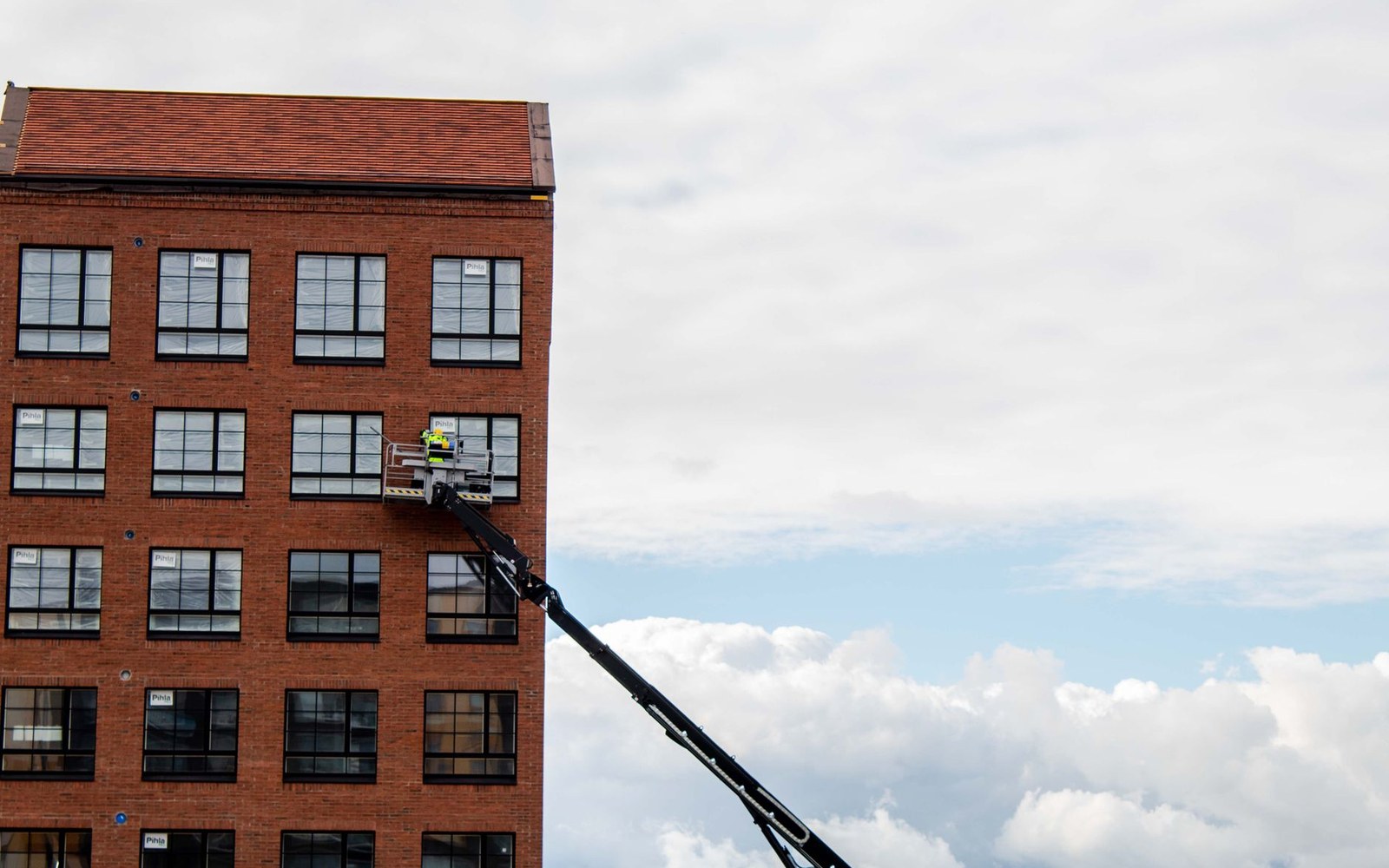 Worker in a raised cherry picker basket beside a tall brick building's windows