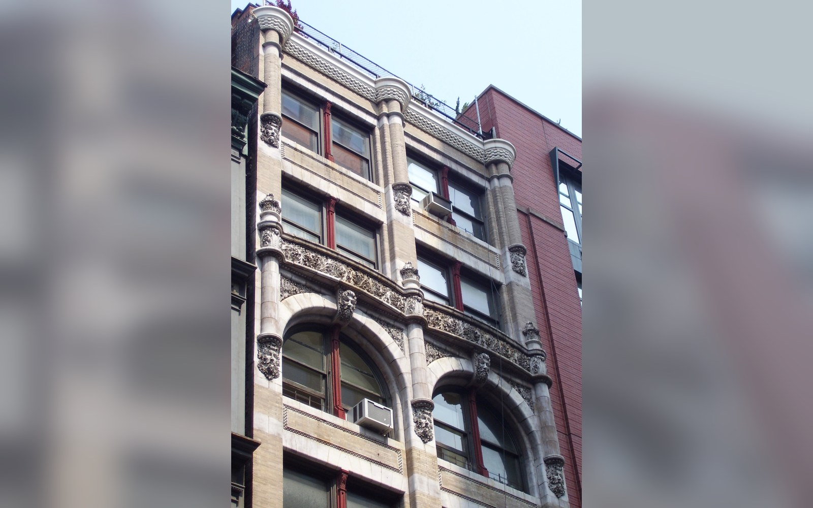 Ornate stone facade with arched windows and carved faces on a narrow city building