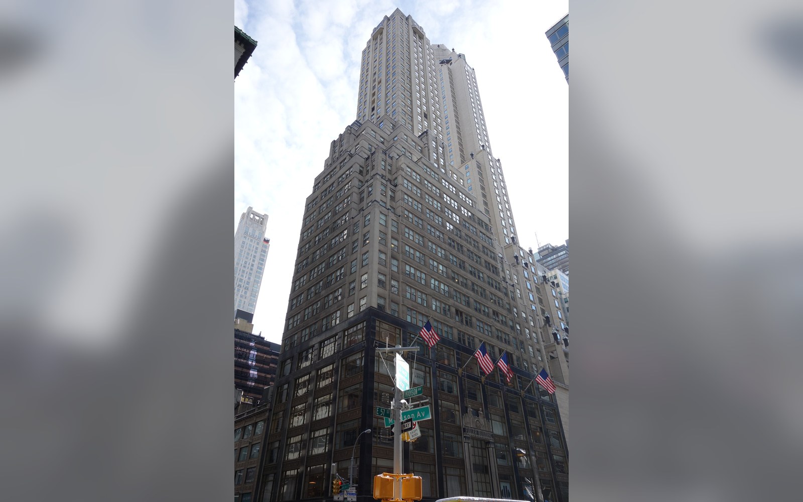 Tall art deco skyscraper with setback tiers rising above a street-level storefront with flags