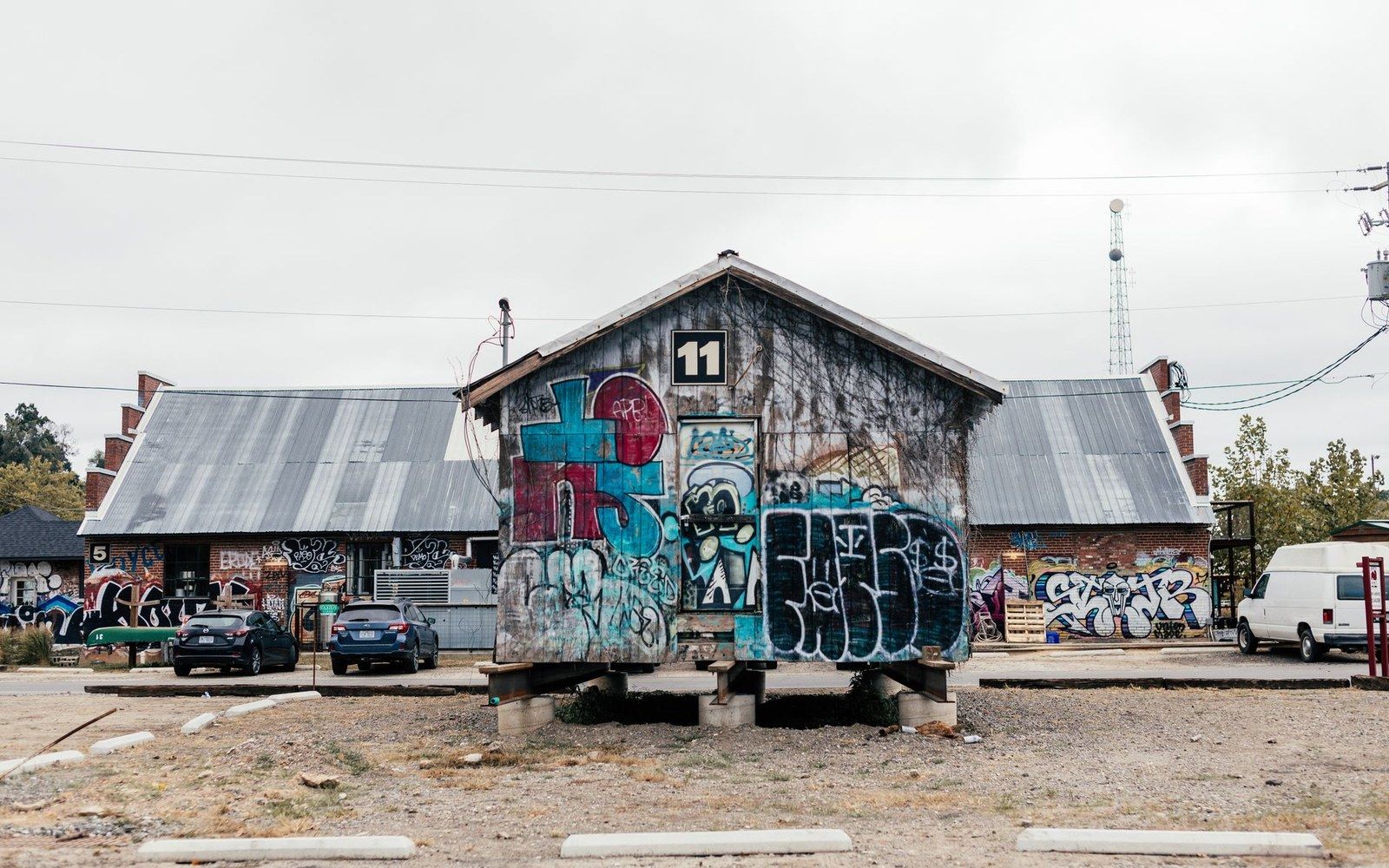 Graffiti-covered warehouse buildings with metal roofs and cars parked outside