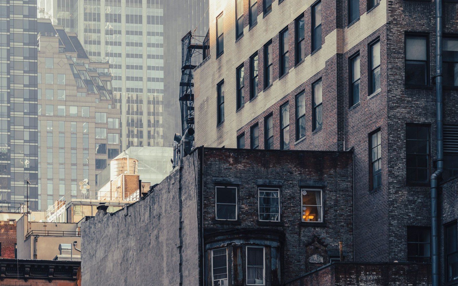 Brick tenement buildings with a rooftop water tower against taller glass skyscrapers behind