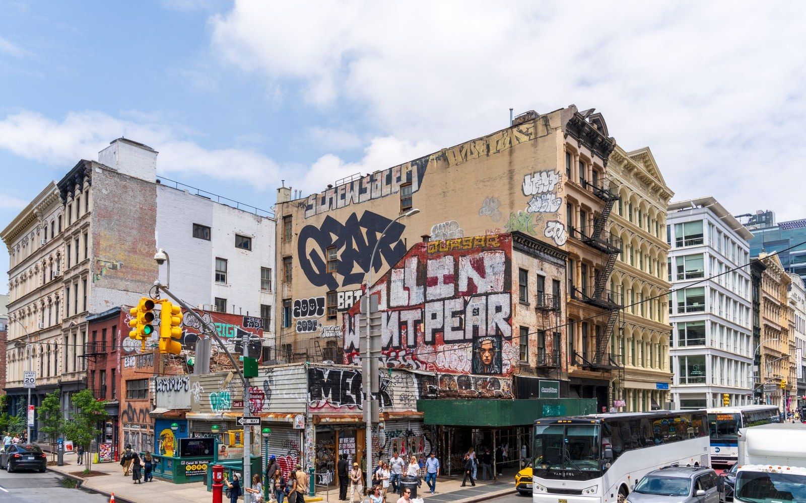 Graffiti-covered cast-iron buildings line a busy SoHo street corner with pedestrians and buses