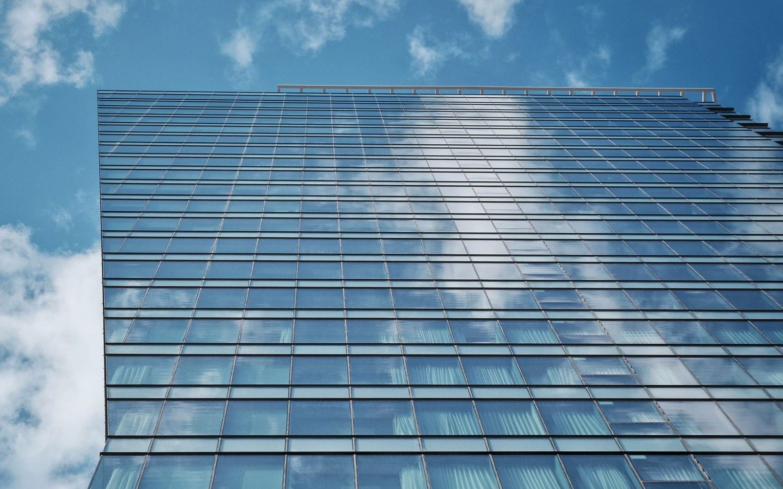 Glass skyscraper facade reflecting clouds, viewed from below at an angle