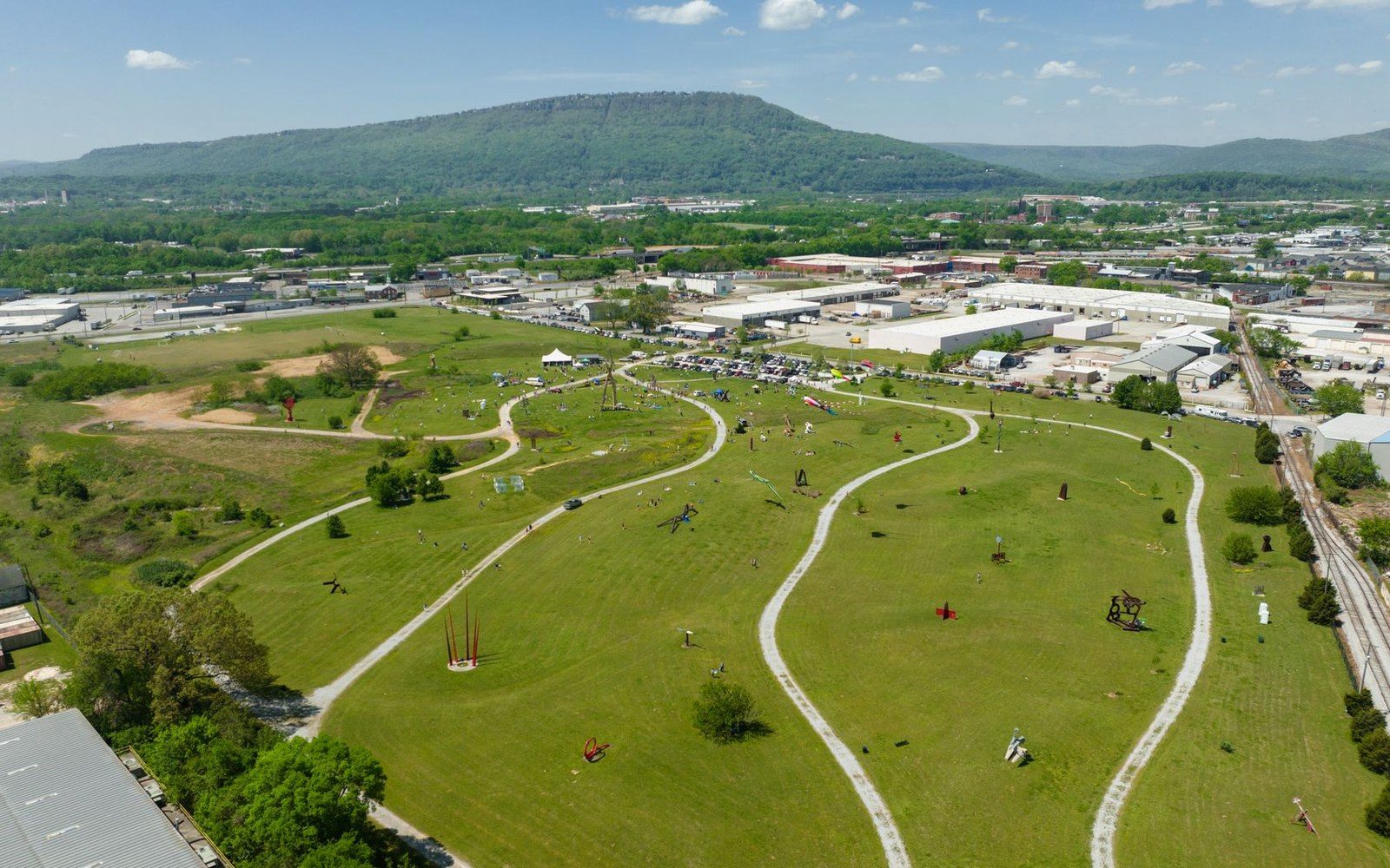 Aerial view of a sculpture park with winding paths across grassy hills below a mountain