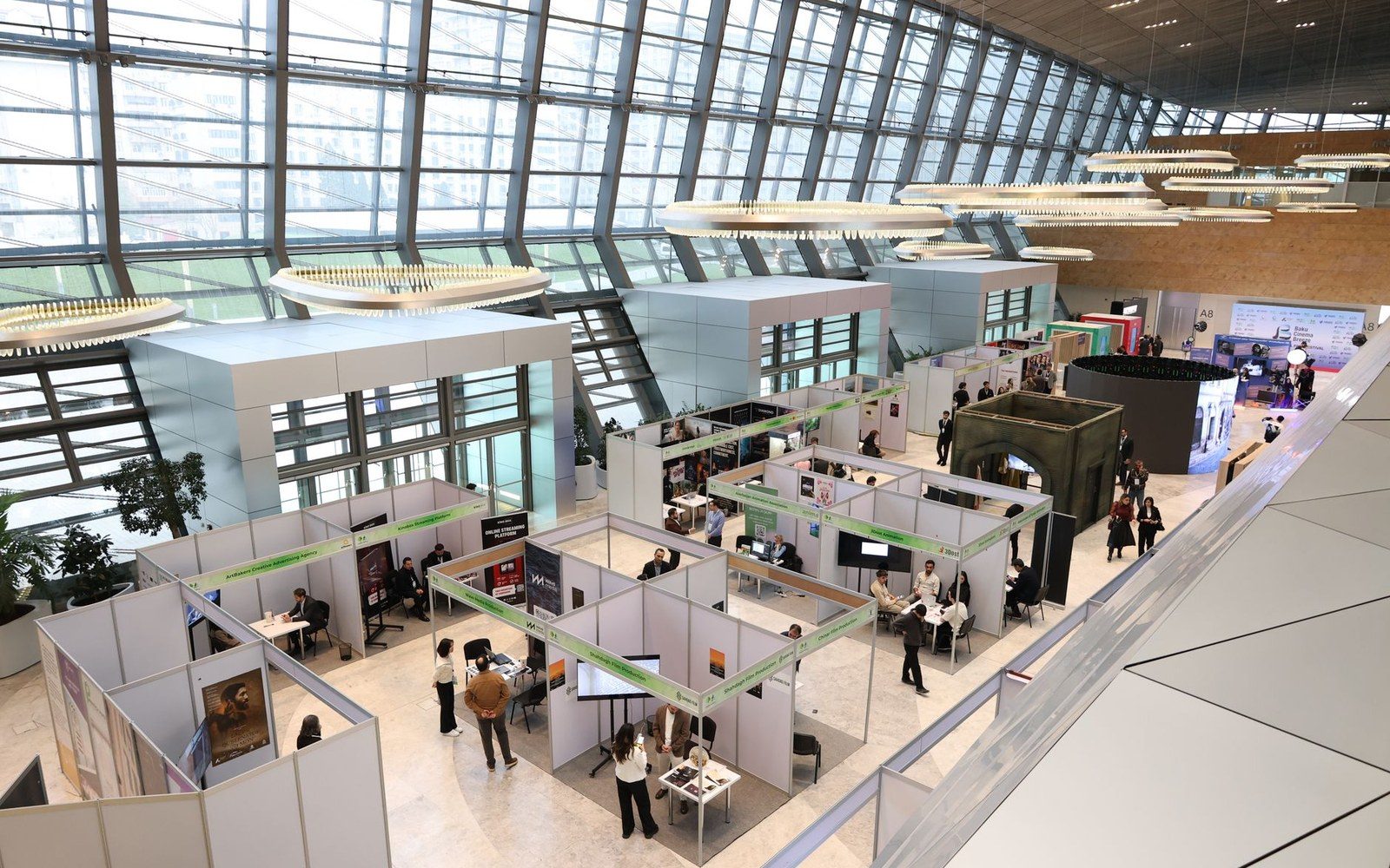 Wide view down an art fair pier hall in full swing — booths either side, adult crowd moving through, large works on temporary partition walls